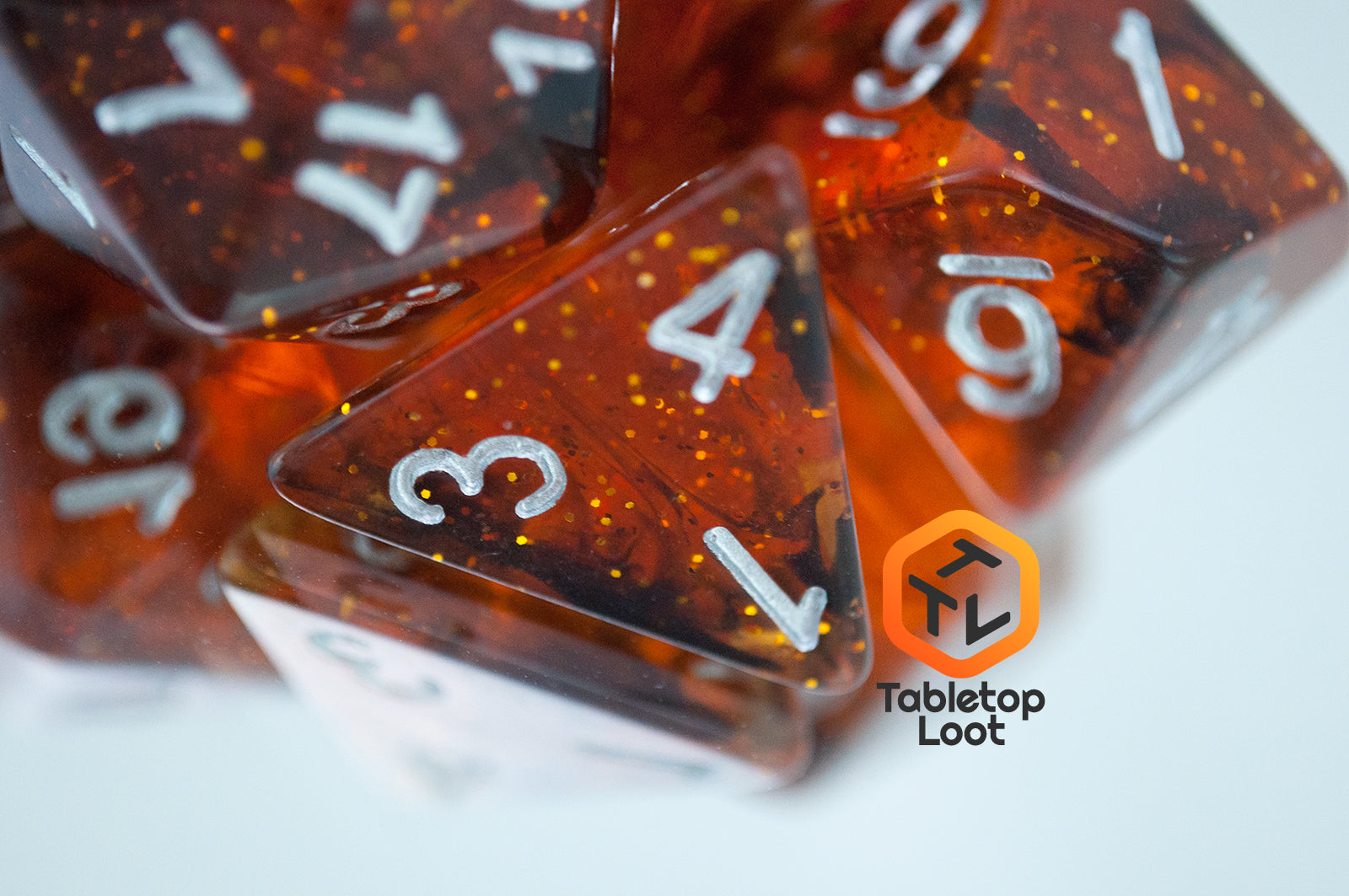 A close up of the Dissonant Whispers 7 piece dice set from Tabletop Loot with swirls of black in sparkling amber color, inked in silver.