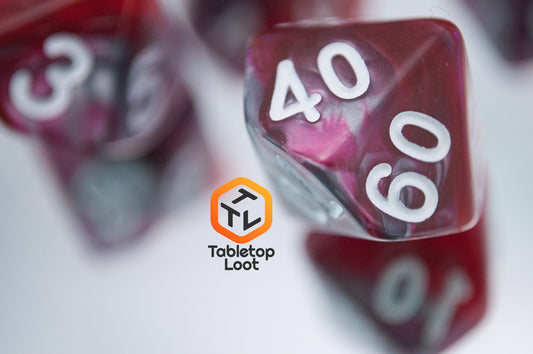 A close up of the percentile die from the Dragon's Blood 7 piece dice set from Tabletop Loot with swirled red and grey resin and white numbering.