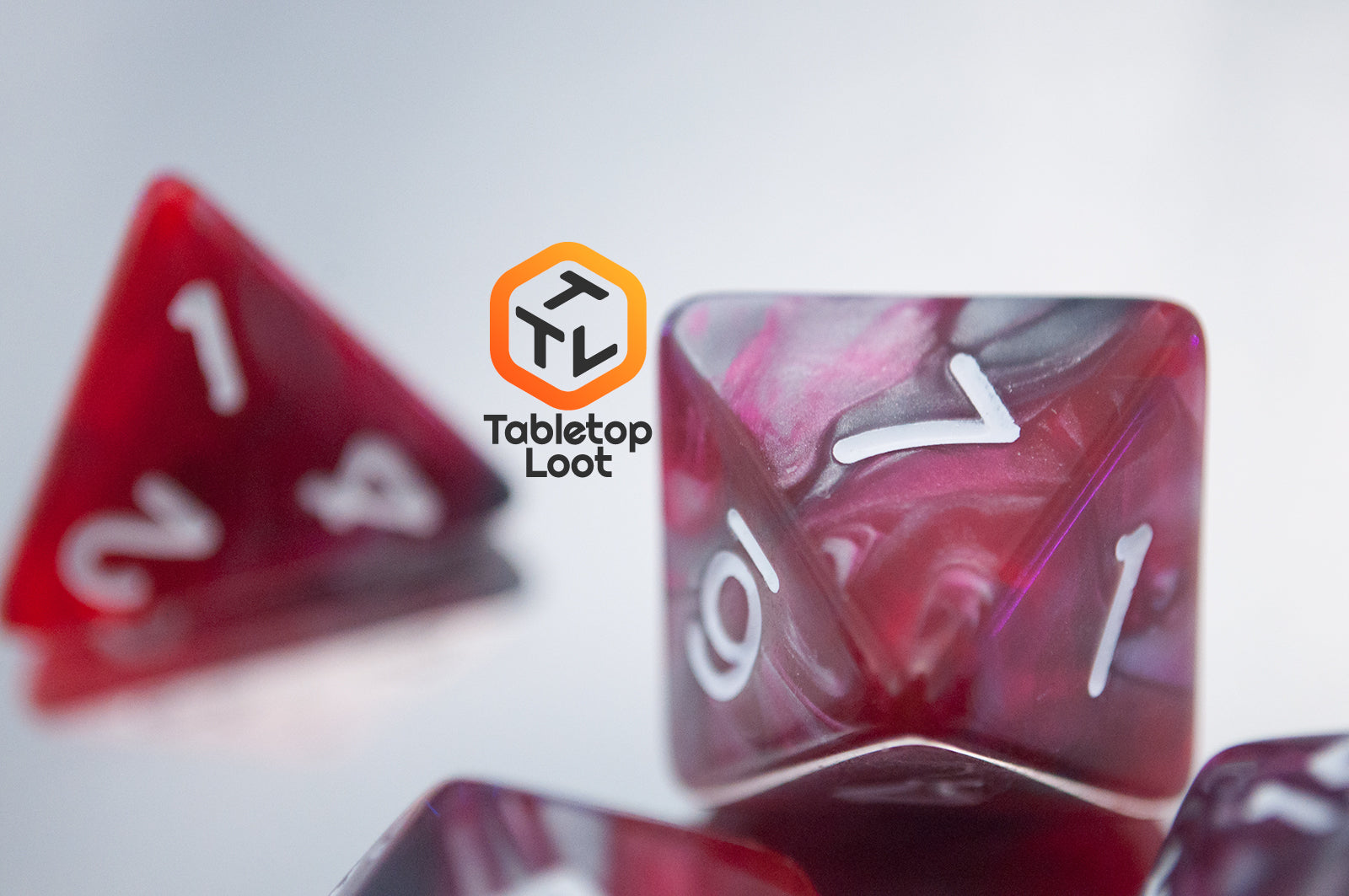 A close up of the Dragon's Blood 7 piece dice set from Tabletop Loot with swirled red and grey resin and white numbering.