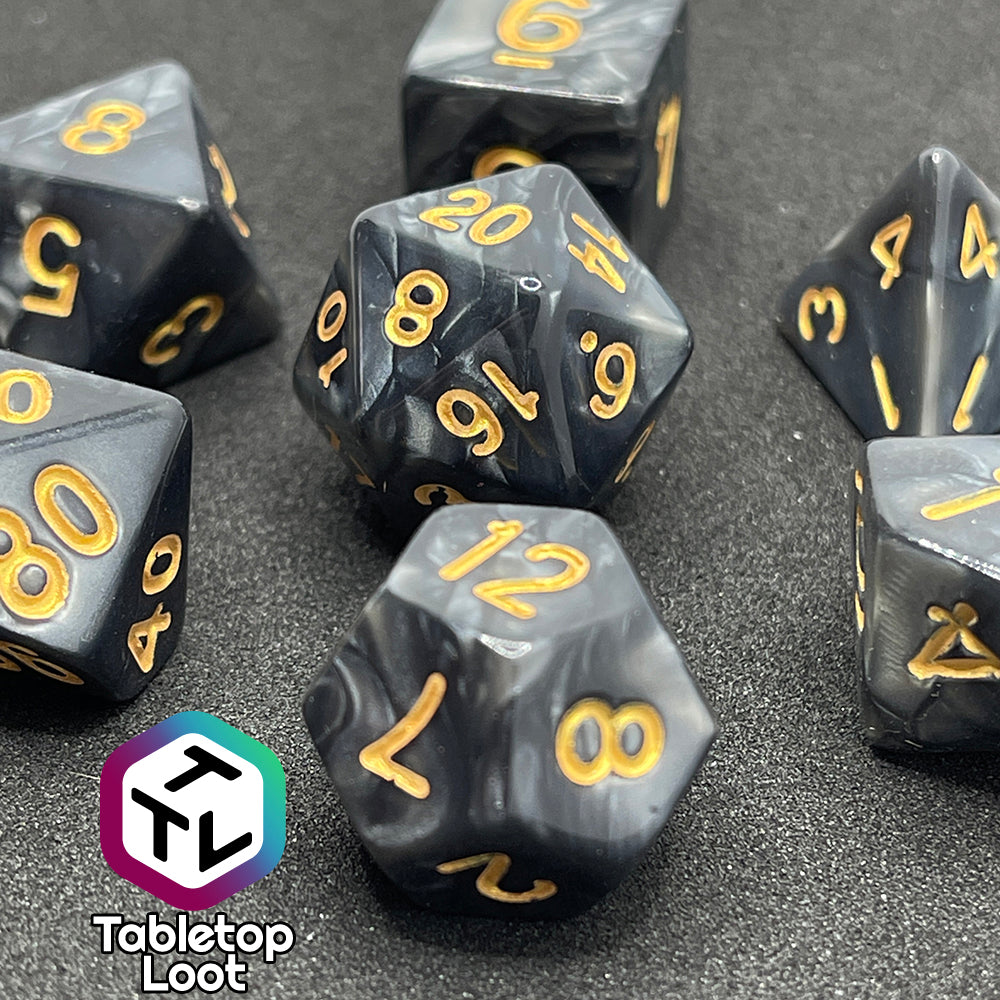 A close up of the Dreadnaught 7 piece dice set from Tabletop Loot with swirls of pearlescent black and gold numbering.