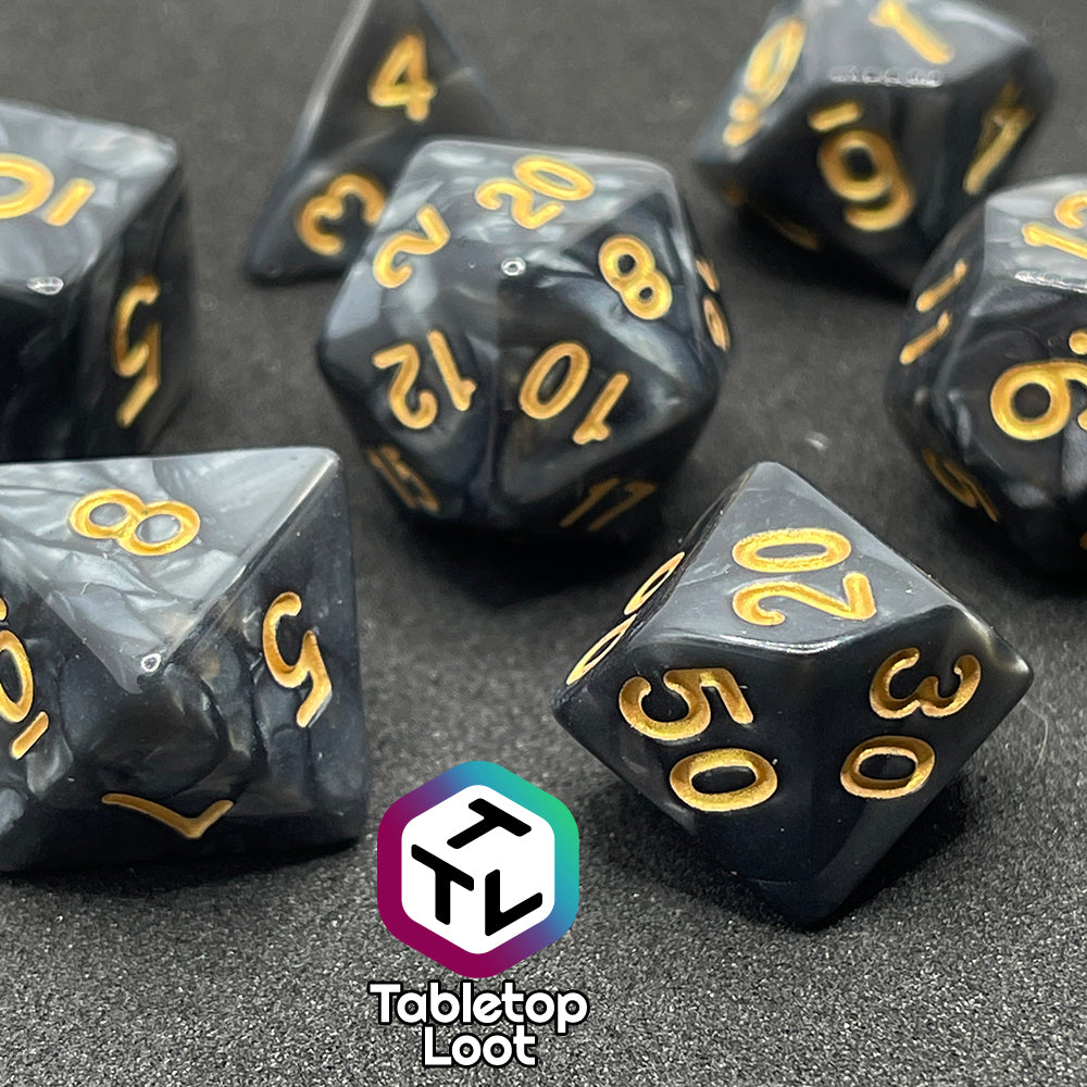 A close up of the Dreadnaught 7 piece dice set from Tabletop Loot with swirls of pearlescent black and gold numbering.