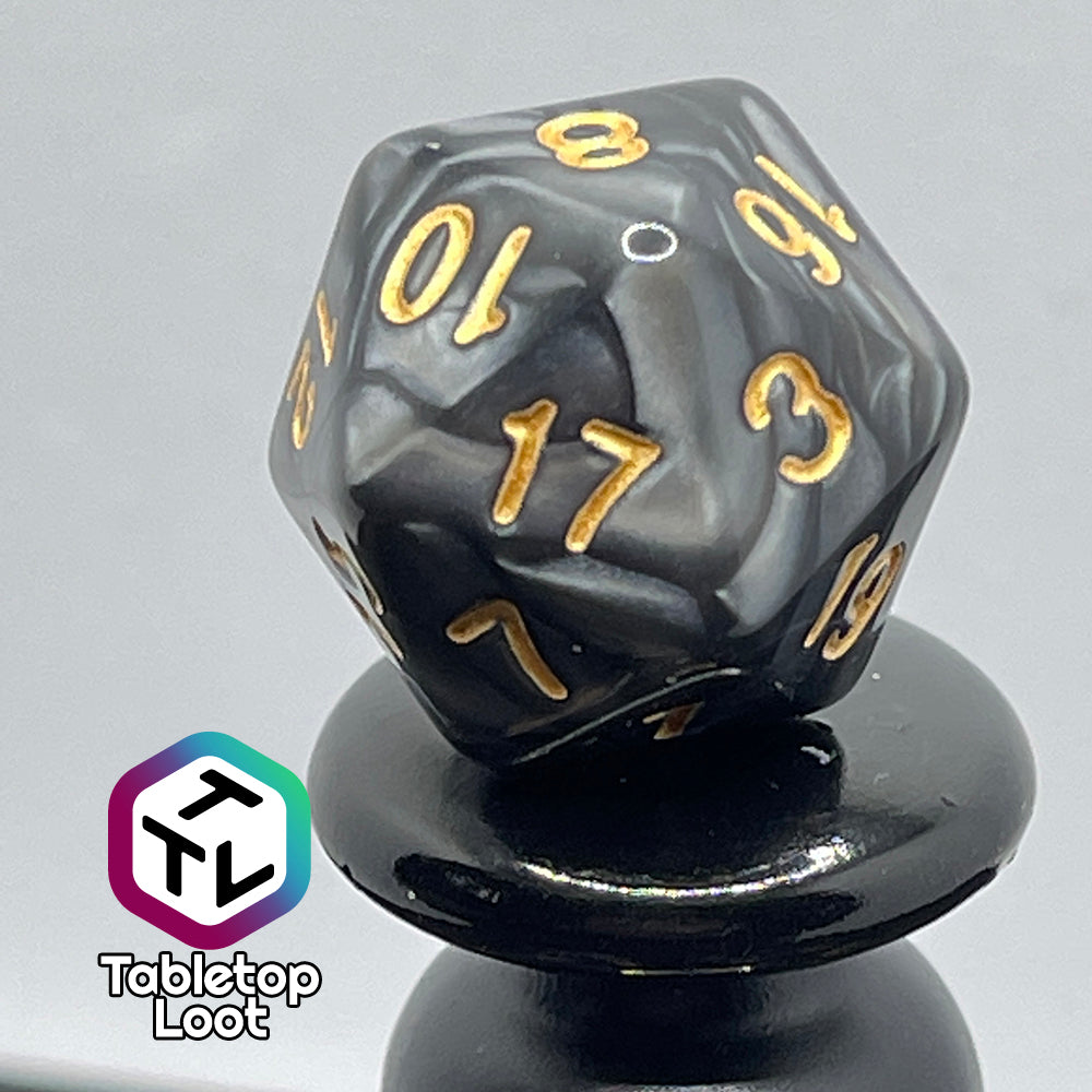 A close up of the D20 from the Dreadnaught 11 piece dice set from Tabletop Loot with swirls of pearlescent black and golden numbering.