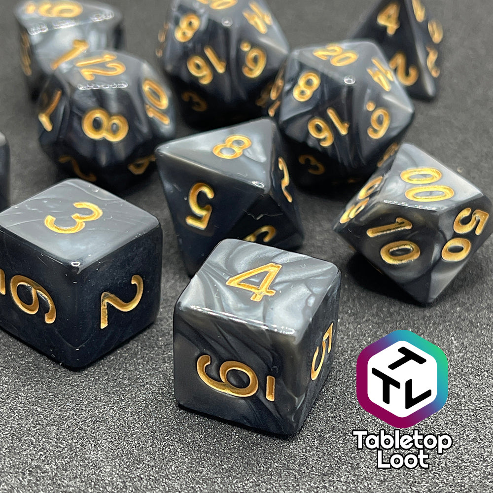 A close up of the Dreadnaught 11 piece dice set from Tabletop Loot with swirls of pearlescent black and golden numbering.