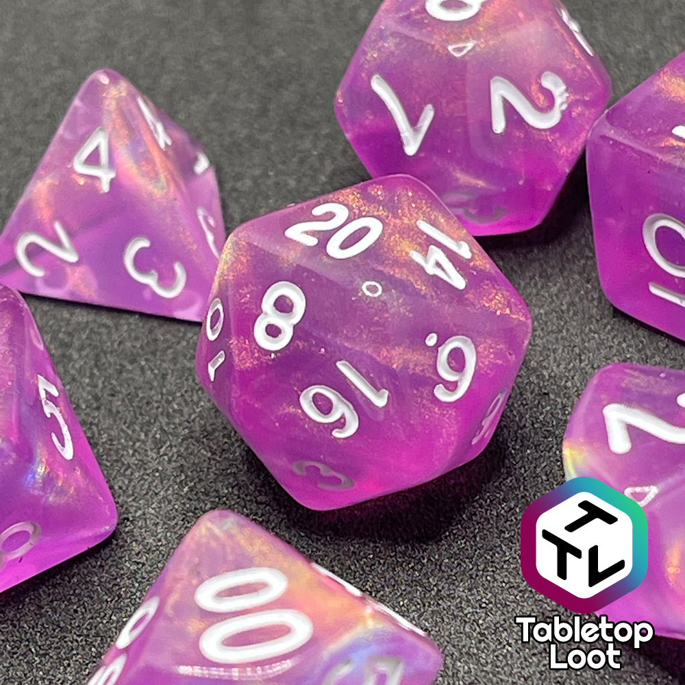 A close up of the Dreamscapes 7 piece dice set from Tabletop Loot; pink with iridescent glitter and white numbering.