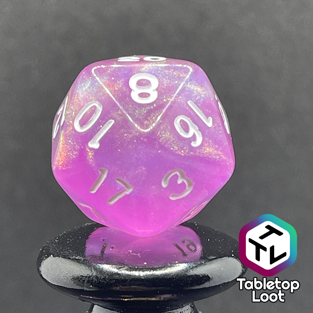 A close up of the D20 from the Dreamscapes 7 piece dice set from Tabletop Loot; pink with iridescent glitter and white numbering.