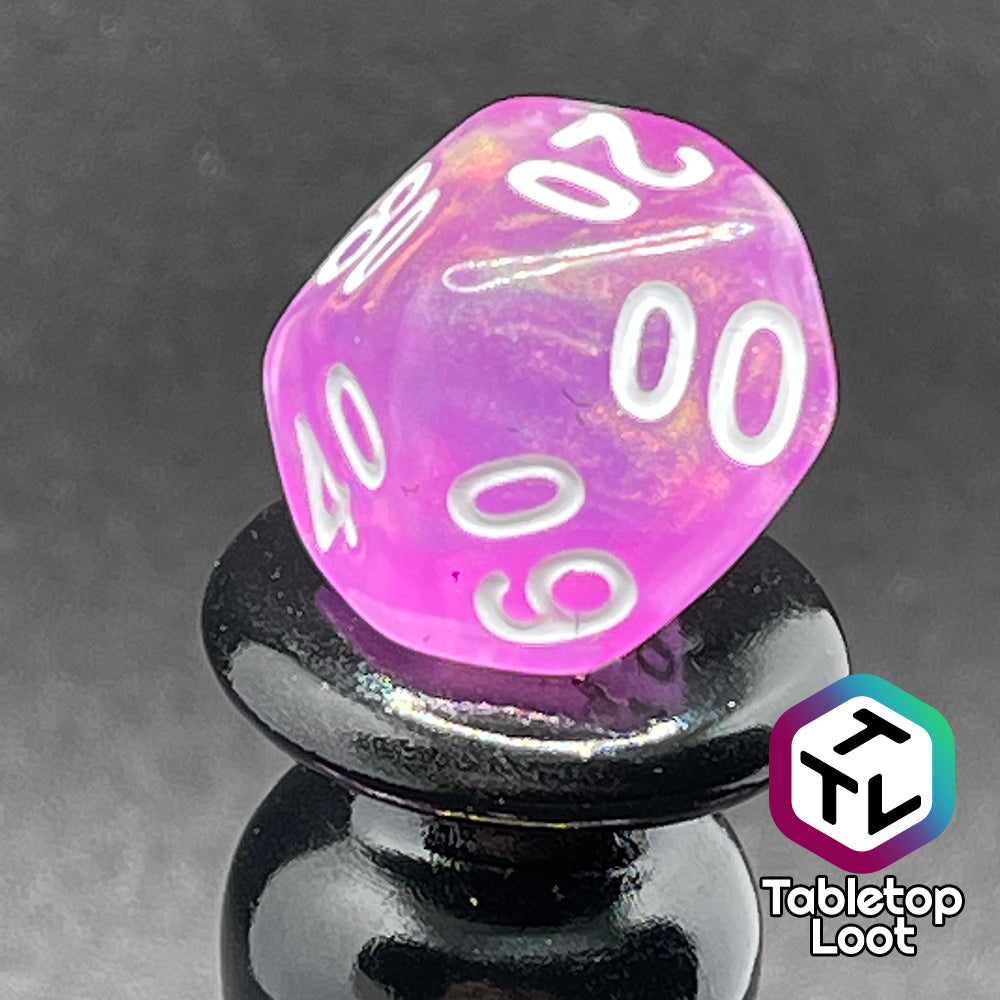 A close up of the percentile die from the Dreamscapes 7 piece dice set from Tabletop Loot; pink with iridescent glitter and white numbering.