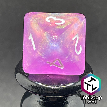 A close up of the D6 from the Dreamscapes 7 piece dice set from Tabletop Loot; pink with iridescent glitter and white numbering.