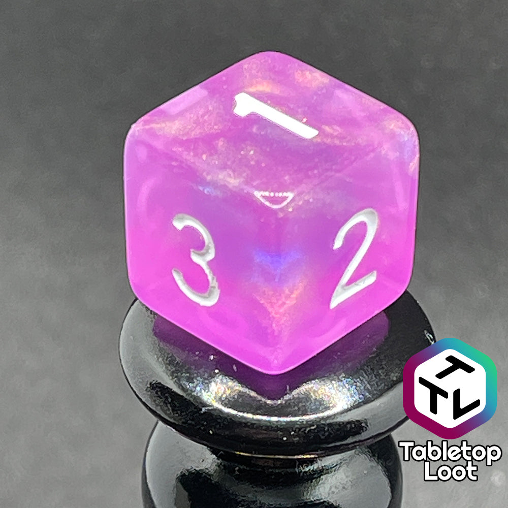 A close up of the D6 from the Dreamscapes 7 piece dice set from Tabletop Loot; pink with iridescent glitter and white numbering.