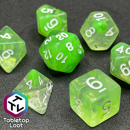 A close up of the Ectoplasm 7 piece dice set from Tabletop Loot with swirls of lime green in clear resin and white numbering.