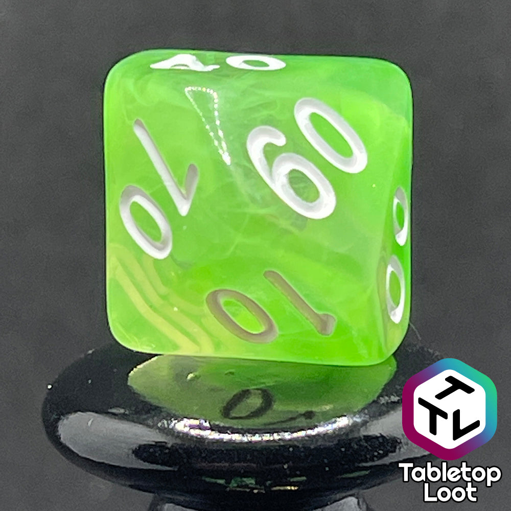 A close up of the percentile die from the Ectoplasm 7 piece dice set from Tabletop Loot with swirls of lime green in clear resin and white numbering.