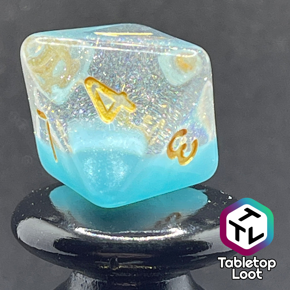A close up of the D8 from the Elsa 7 piece dice set from Tabletop Loot with a layer of sky blue under glittery clear resin and golden numbering.