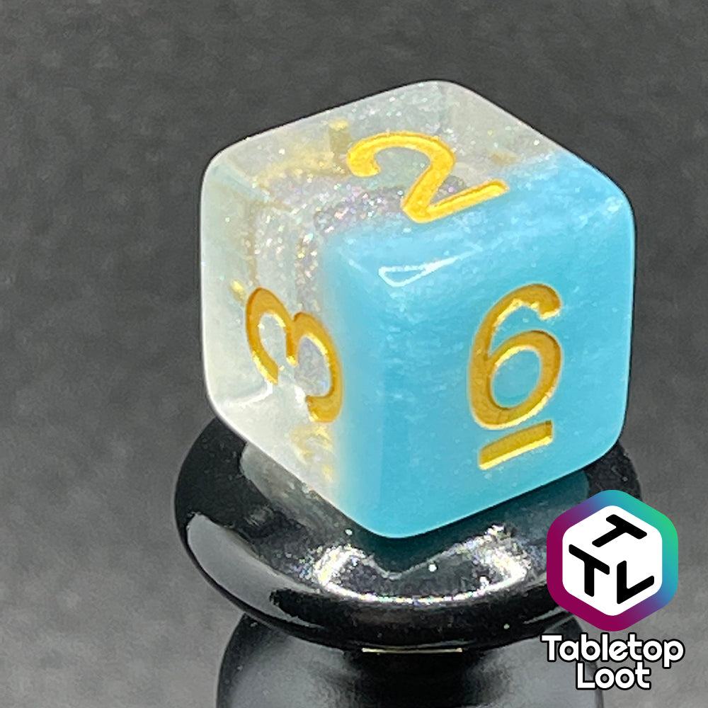 A close up of the D6 from the Elsa 7 piece dice set from Tabletop Loot with a layer of sky blue under glittery clear resin and golden numbering.