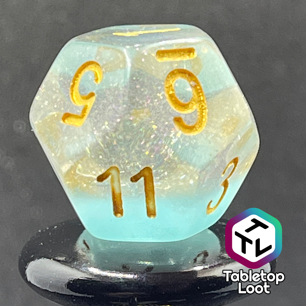 A close up of the D12 from the Elsa 7 piece dice set from Tabletop Loot with a layer of sky blue under glittery clear resin and golden numbering.