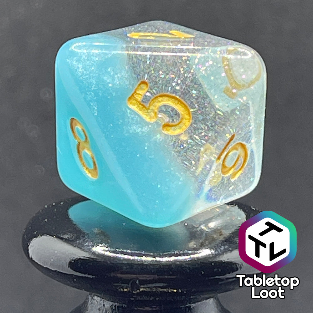 A close up of the D8 from the Elsa 7 piece dice set from Tabletop Loot with a layer of sky blue under glittery clear resin and golden numbering.