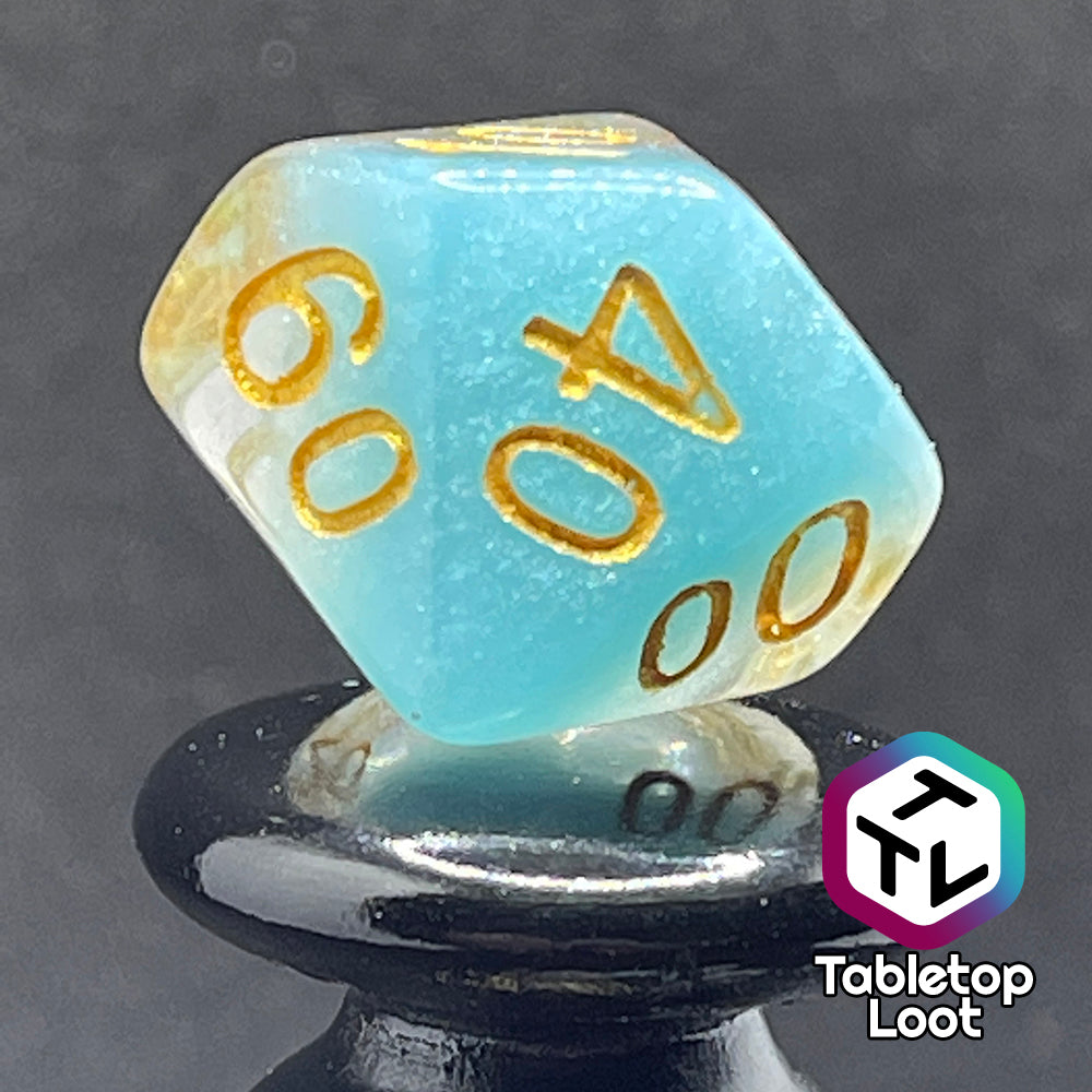 A close up of the percentile die from the Elsa 7 piece dice set from Tabletop Loot with a layer of sky blue under glittery clear resin and golden numbering.