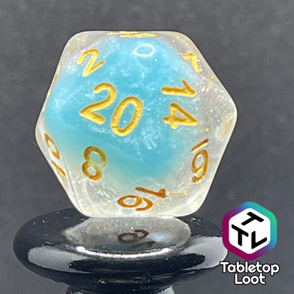 A close up of the D20 from the Elsa 7 piece dice set from Tabletop Loot with a layer of sky blue under glittery clear resin and golden numbering.