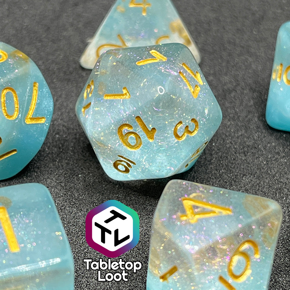 A close up of the Elsa 7 piece dice set from Tabletop Loot with a layer of sky blue under glittery clear resin and golden numbering.