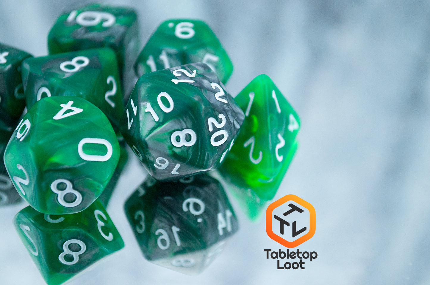 A close up of the Emerald Ore 7 piece dice set from Tabletop Loot with swirls of green and silver resin and white numbering.