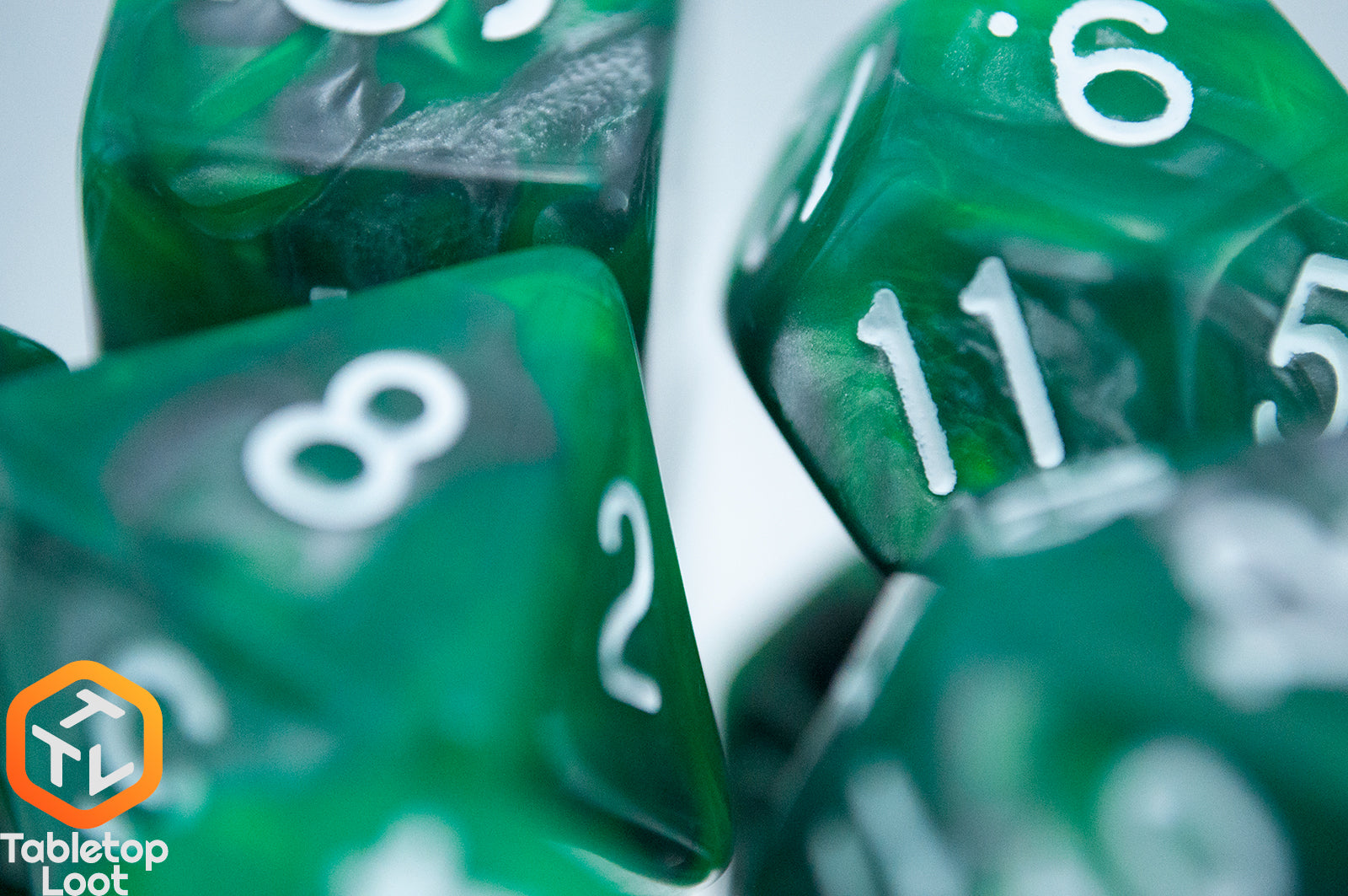 A close up of the Emerald Ore 7 piece dice set from Tabletop Loot with swirls of green and silver resin and white numbering.