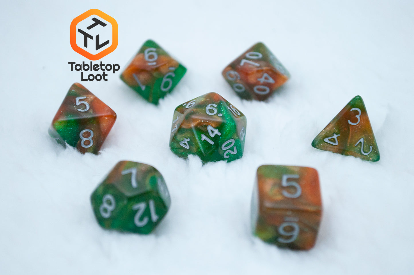 The Emerald Vale 7 piece dice set from Tabletop Loot with swirls of orange in green resin, lots of sparkle, and white numbering.