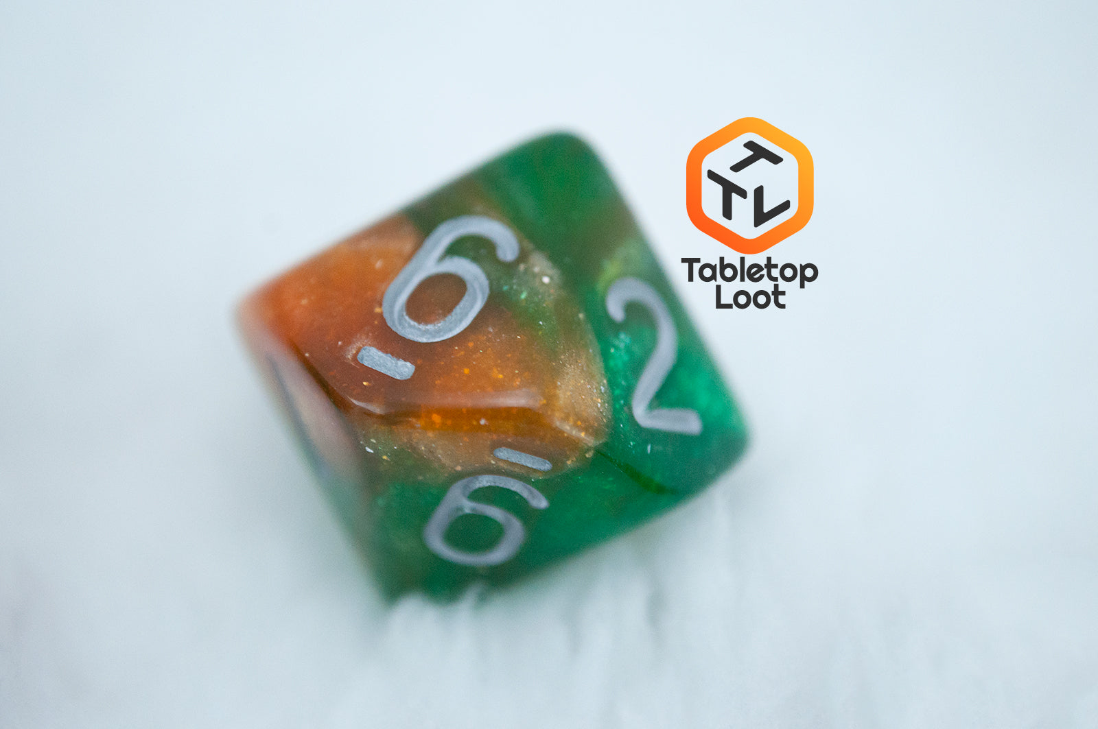 A close up of the D10 from the Emerald Vale 7 piece dice set from Tabletop Loot with swirls of orange in green resin, lots of sparkle, and white numbering.