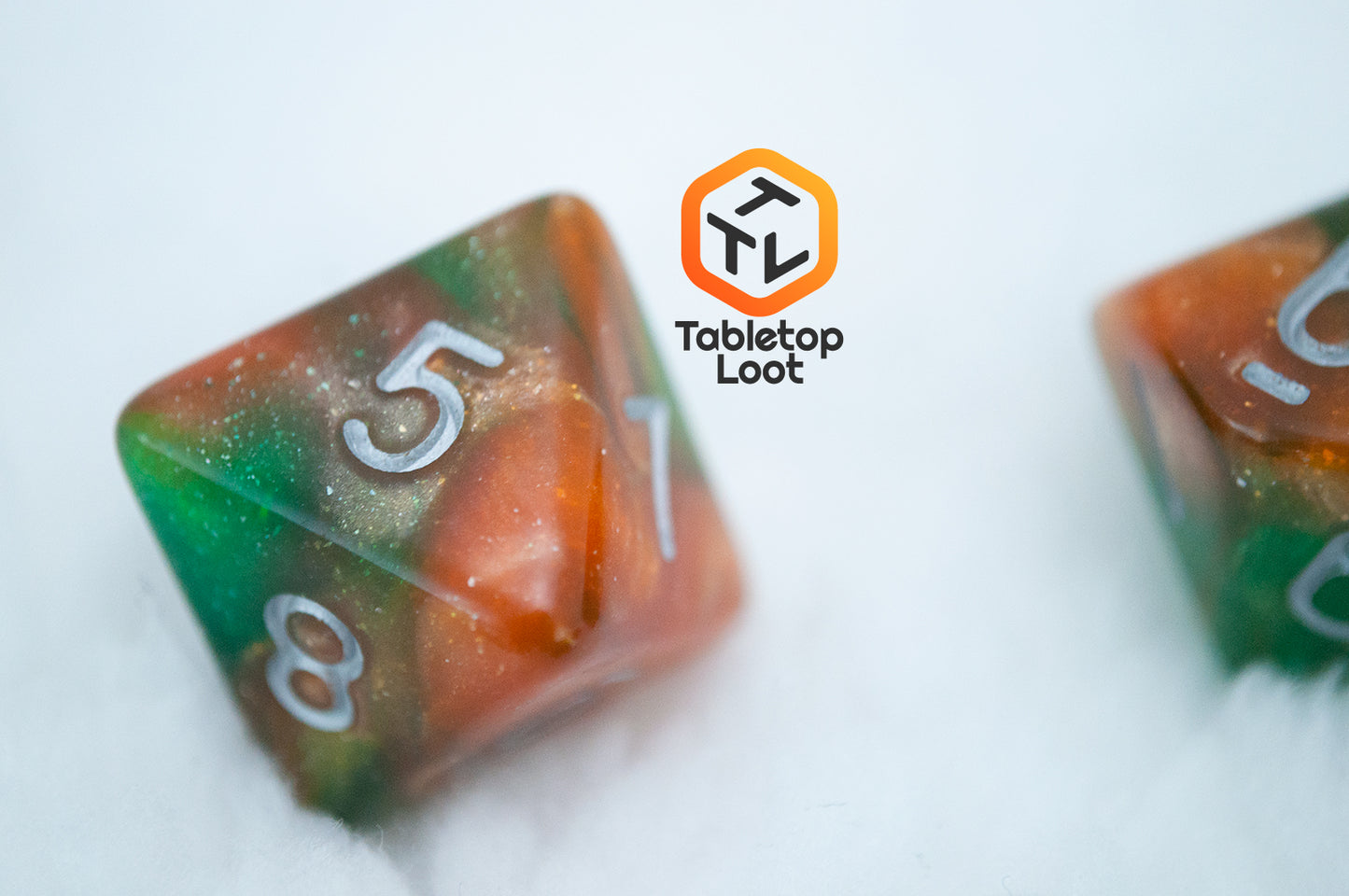 A close up of the D8 from the Emerald Vale 7 piece dice set from Tabletop Loot with swirls of orange in green resin, lots of sparkle, and white numbering.