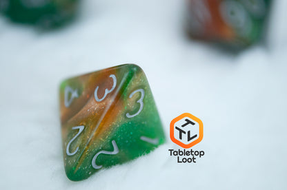 A close up of the D4 from the Emerald Vale 7 piece dice set from Tabletop Loot with swirls of orange in green resin, lots of sparkle, and white numbering.