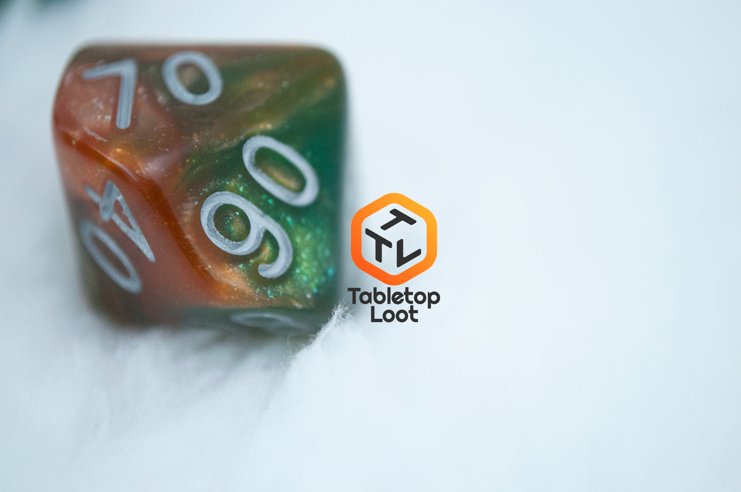 A close up of the D10 from the Emerald Vale 7 piece dice set from Tabletop Loot with swirls of orange in green resin, lots of sparkle, and white numbering.