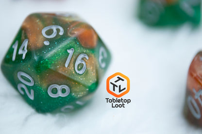 A close up of the Emerald Vale D20 from Tabletop Loot with swirls of orange in green resin, lots of sparkle, and white numbering.
