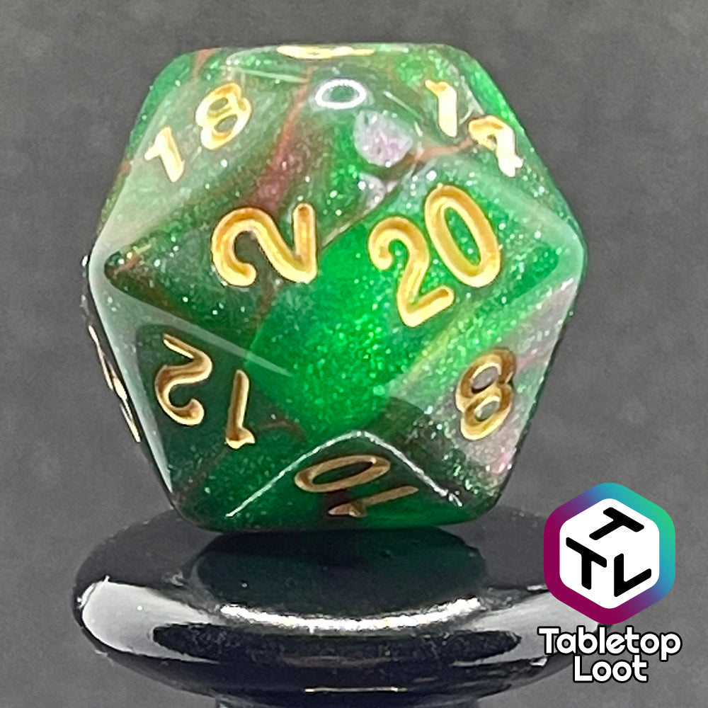 A close up of the D20 from the Enchanted Forest 7 piece dice set from Tabletop Loot with swirls of pink and green glittery resin and gold numbering.