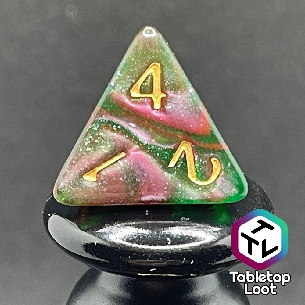 A close up of the D4 from the Enchanted Forest 7 piece dice set from Tabletop Loot with swirls of pink and green glittery resin and gold numbering.