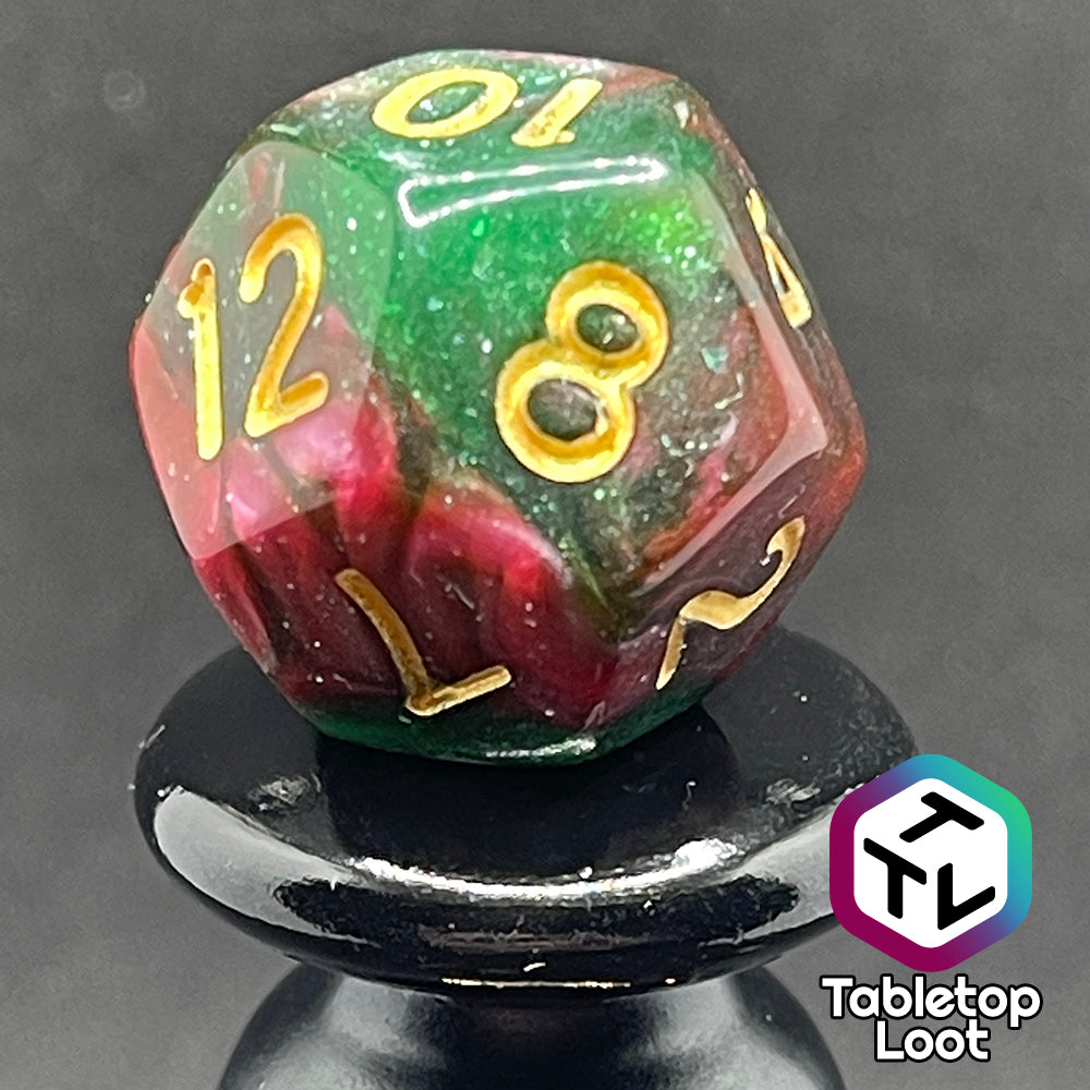 A close up of the D12 from the Enchanted Forest 7 piece dice set from Tabletop Loot with swirls of pink and green glittery resin and gold numbering.