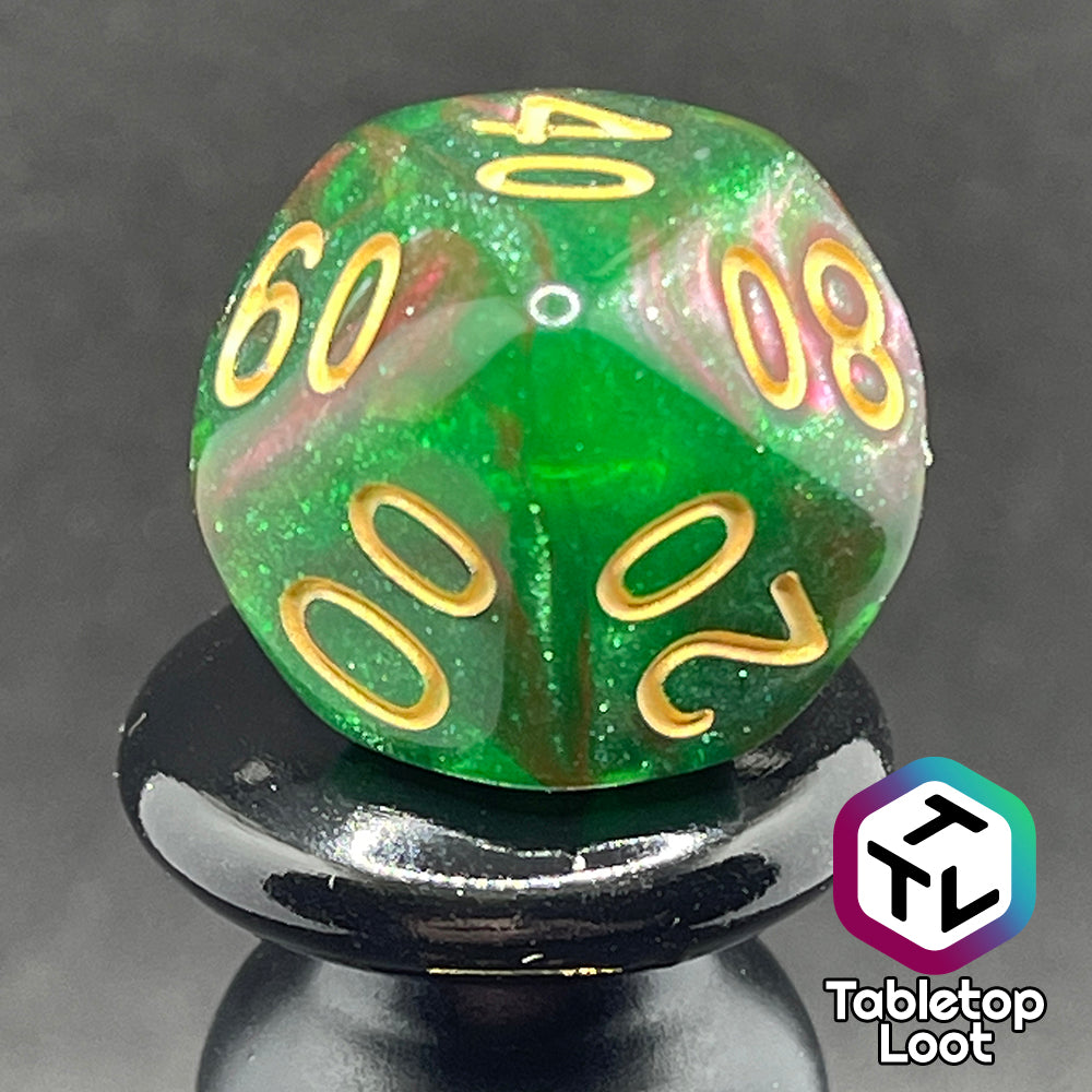 A close up of the percentile die from the Enchanted Forest 7 piece dice set from Tabletop Loot with swirls of pink and green glittery resin and gold numbering.