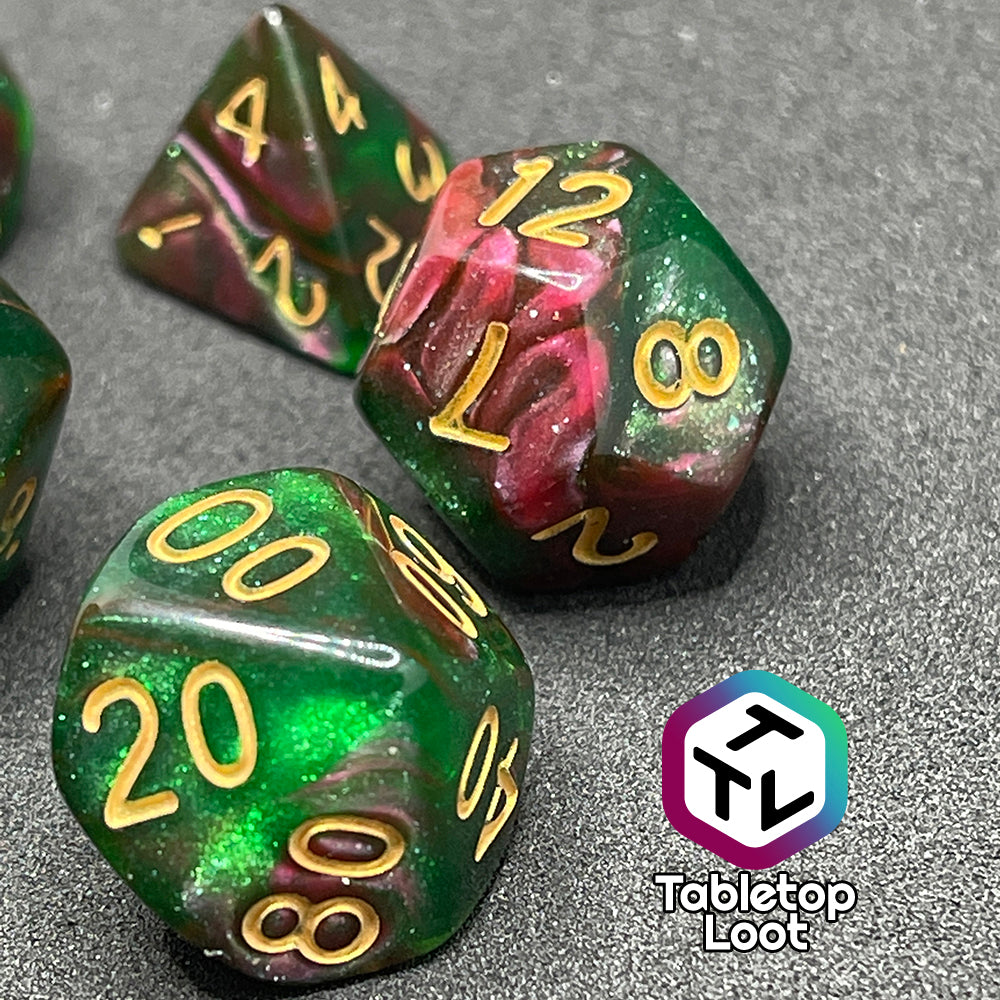 A close up of the D12 and percentile die from the Enchanted Forest 7 piece dice set from Tabletop Loot with swirls of pink and green glittery resin and gold numbering.