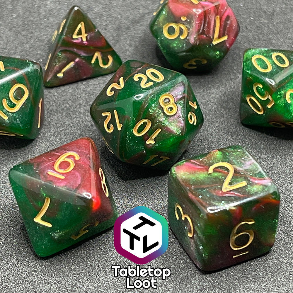 A close up of the Enchanted Forest 7 piece dice set from Tabletop Loot with swirls of pink and green glittery resin and gold numbering.