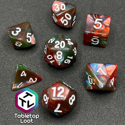 The Ether Stone 7 piece dice set from Tabletop Loot with glittering and pearlescent swirls of red, green, blue, and golden brown with white numbering.