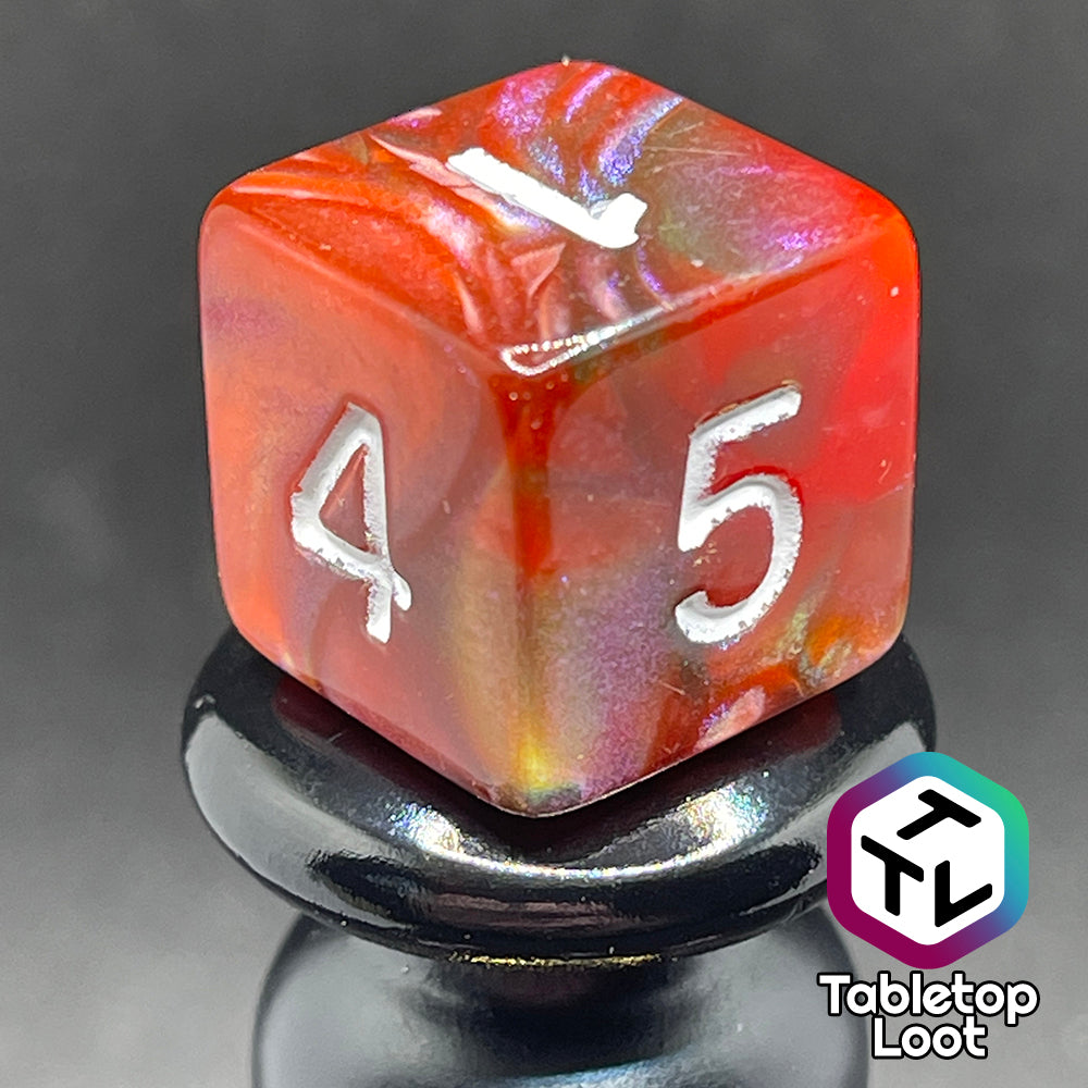 A close up of the D6 from the Ether Stone 7 piece dice set from Tabletop Loot with glittering and pearlescent swirls of red, green, blue, and golden brown with white numbering.