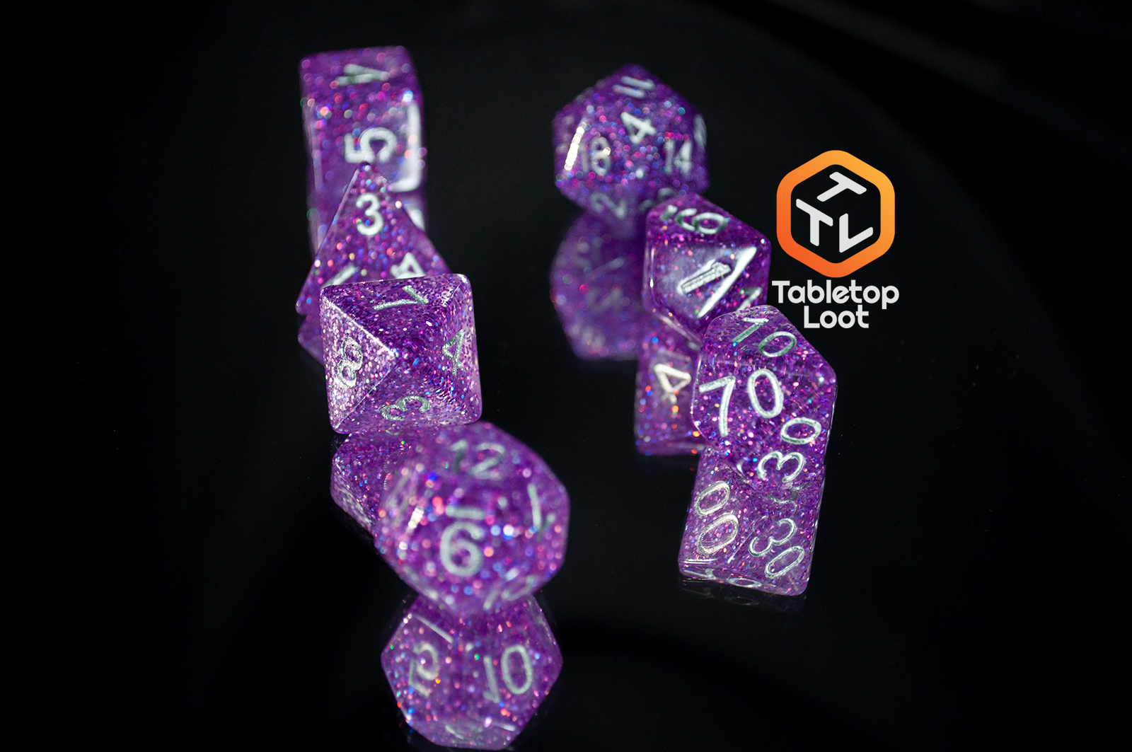 The Faerie Fire 7 piece dice set from Tabletop Loot packed with purple and blue iridescent sparkles in translucent purple with silver numbering.