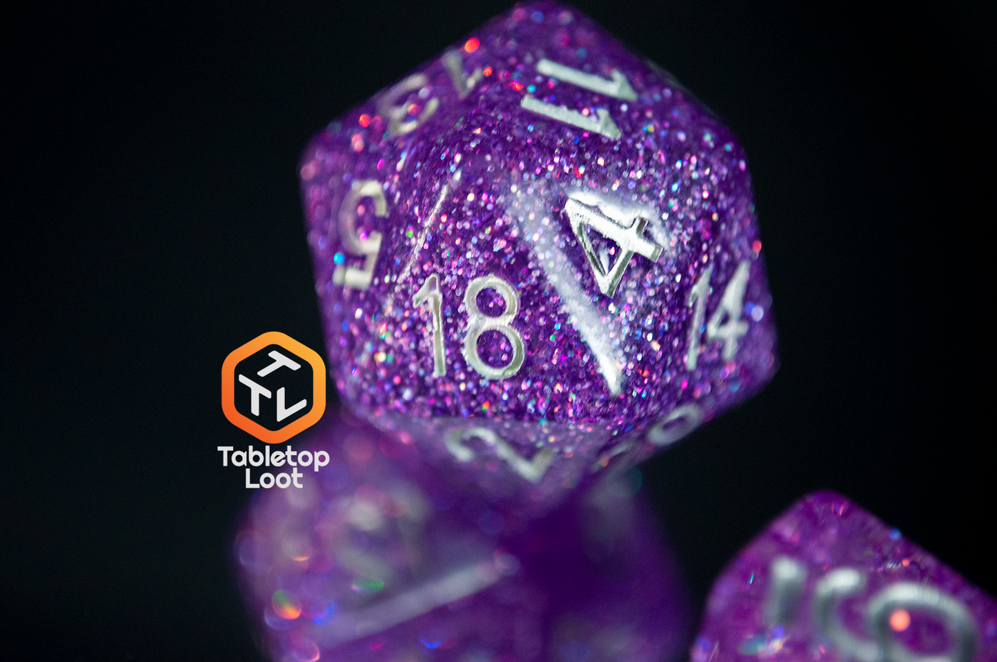 A close up of the D20 from the Faerie Fire 7 piece dice set from Tabletop Loot packed with purple and blue iridescent sparkles in translucent purple with silver numbering.
