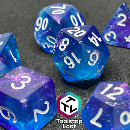 A close up of the Fathomless 7 piece dice set from Tabletop Loot with swirls of glitter and purple in deep blue and white numbering.