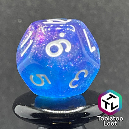 A close up of the D12 from the Fathomless 7 piece dice set from Tabletop Loot with swirls of glitter and purple in deep blue and white numbering.