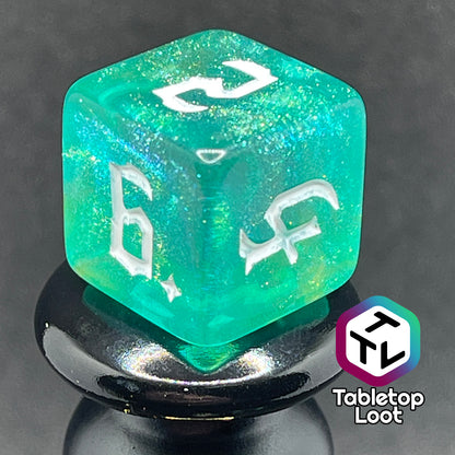 A close up of the D6 from the Fey Moss 7 piece dice set from Tabletop Loot with swirls of glittery green and yellow and white bold gothic numbering.