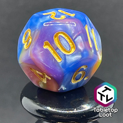 A close up of the D12 from the Fey and Flowers 7 piece dice set with swirls of pearlescent shades of yellow, purple, red, blue, and green and gold numbering.