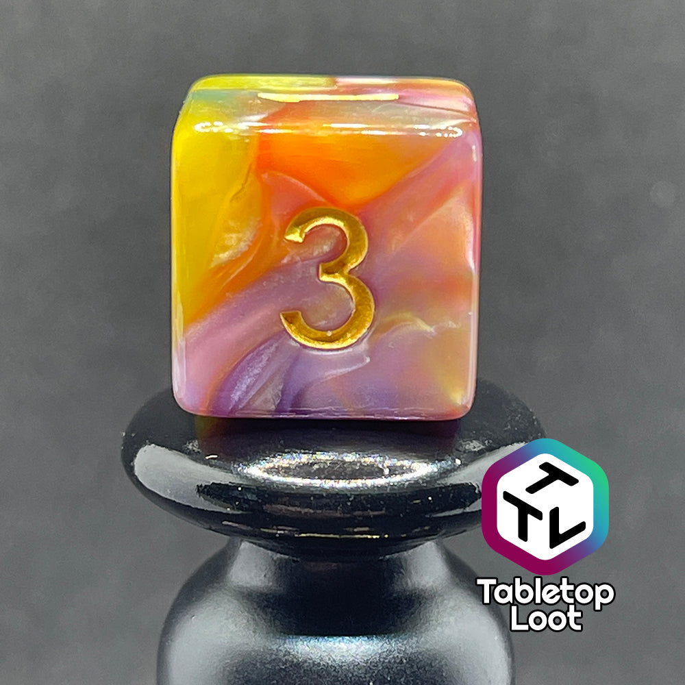 A close up of the D6 from the Fey and Flowers 7 piece dice set with swirls of pearlescent shades of yellow, purple, red, blue, and green and gold numbering.