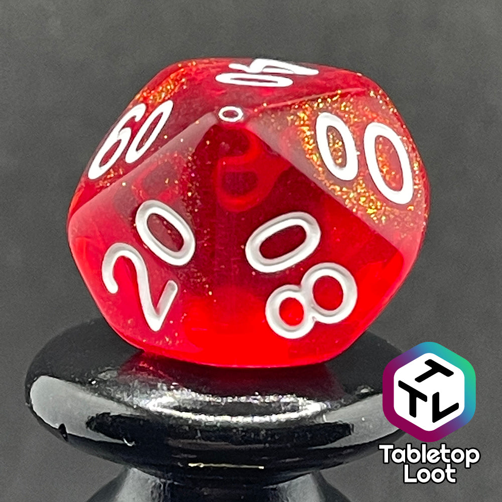 A close up of the percentile die from the Fire Genasi 7 piece dice set from Tabletop Loot with swirls of gold micro glitter in red with white numbering.