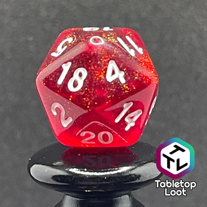 A close up of the D20 from the Fire Genasi 7 piece dice set from Tabletop Loot with swirls of gold micro glitter in red with white numbering.