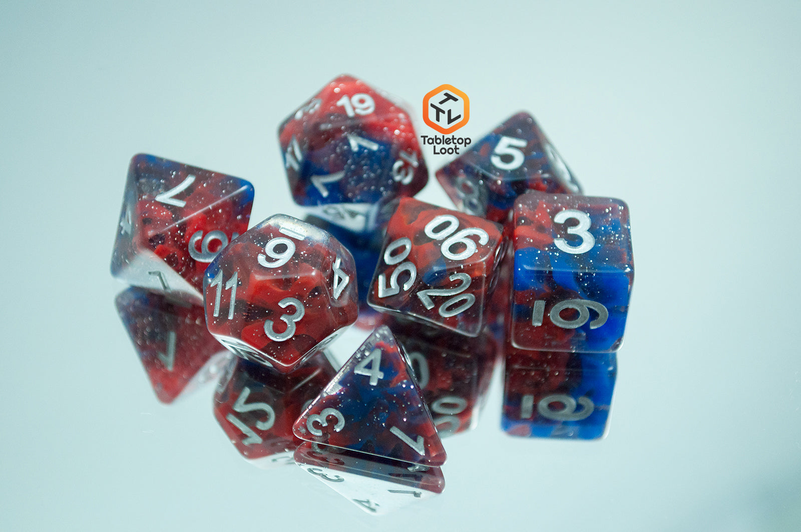 The Fire and Ice 7 piece dice set from Tabletop Loot with swirls of blue and red in a clear glittery resin and silver numbering.
