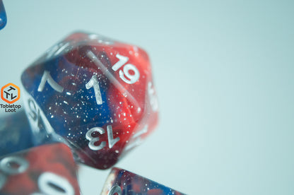 A close up of the D20 from the Fire and Ice 7 piece dice set from Tabletop Loot with swirls of blue and red in a clear glittery resin and silver numbering.