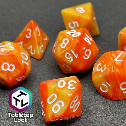 A close up of the Fireball 7 piece dice set from Tabletop Loot, swirling with yellow and orange and inked in white.