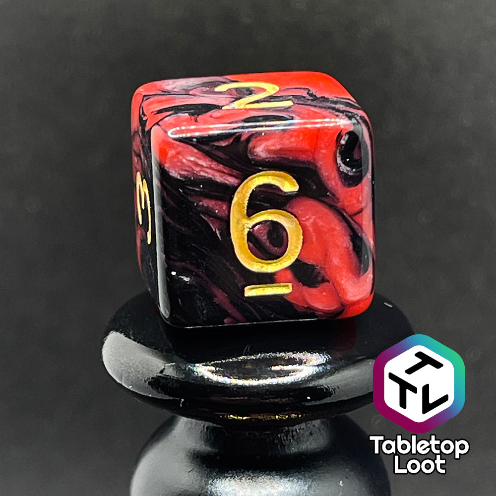 A close up of the D6 from the Forge Embers 7 piece dice set with swirled black and red and gold numbering.